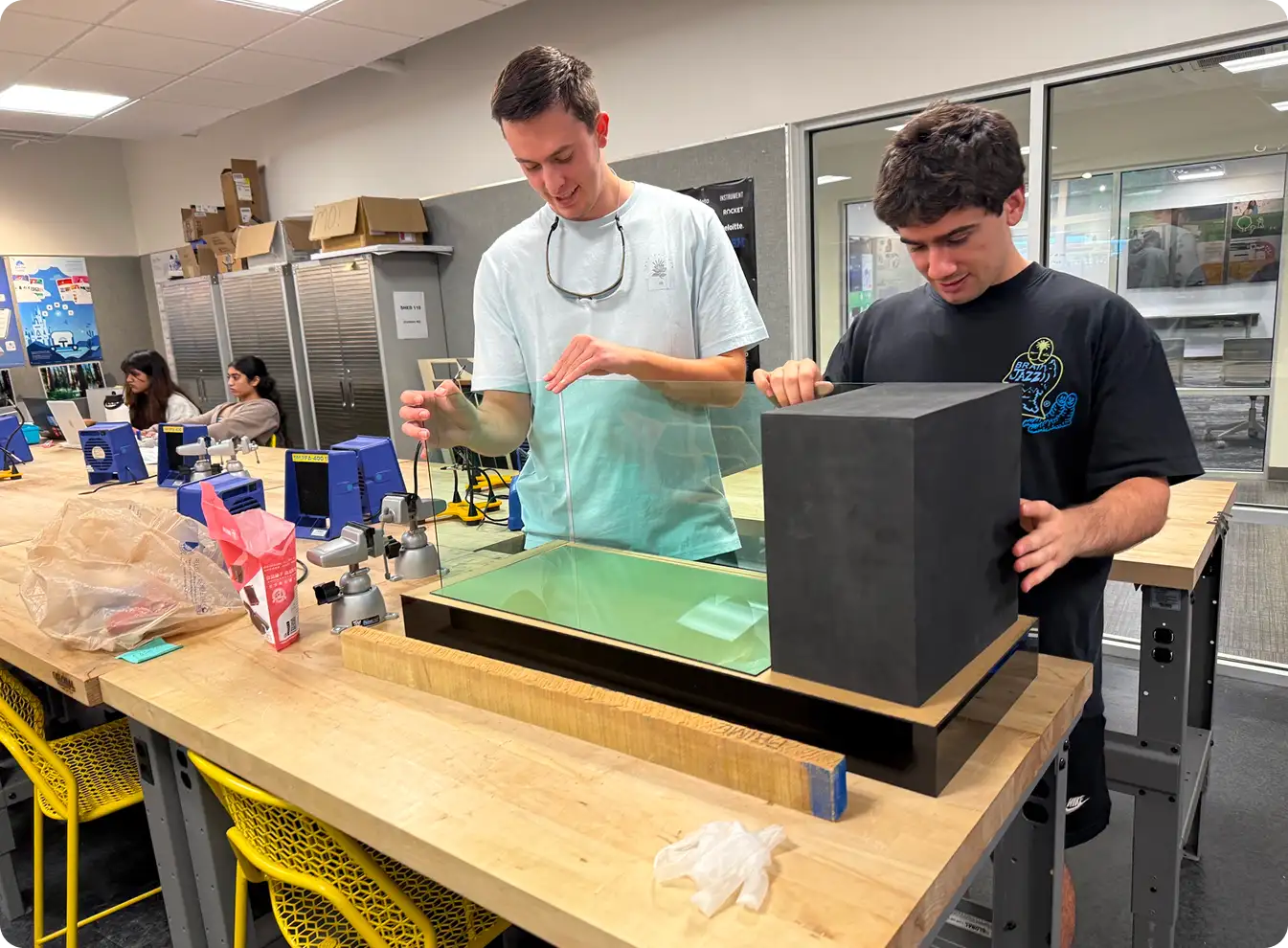 Two team members assembling the acrylic tank housing on a workbench in the fabrication shop